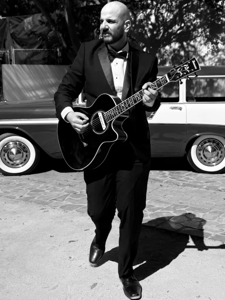 J. Daniel performing wedding guitar in formal attire beside a vintage car